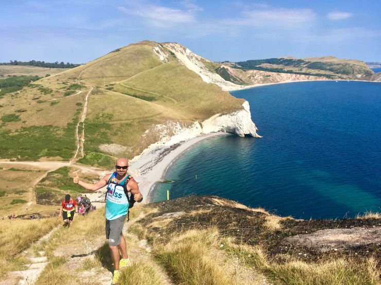 Man wearing Bliss top posing on the coast path with amazing sea views behind him