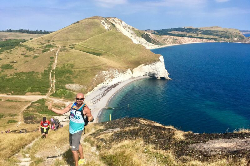 Man wearing Bliss top posing on the coast path with amazing sea views behind him