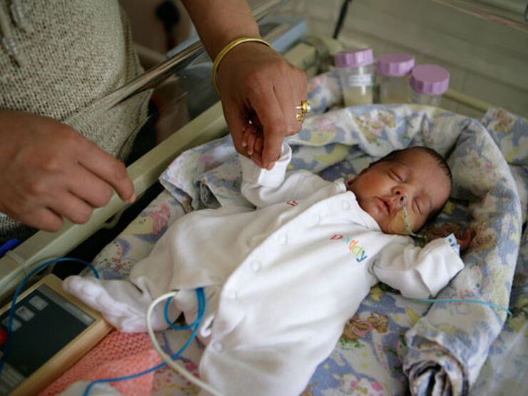 Baby in pyjamas sleeping on its back while parent standing over and holding its hand