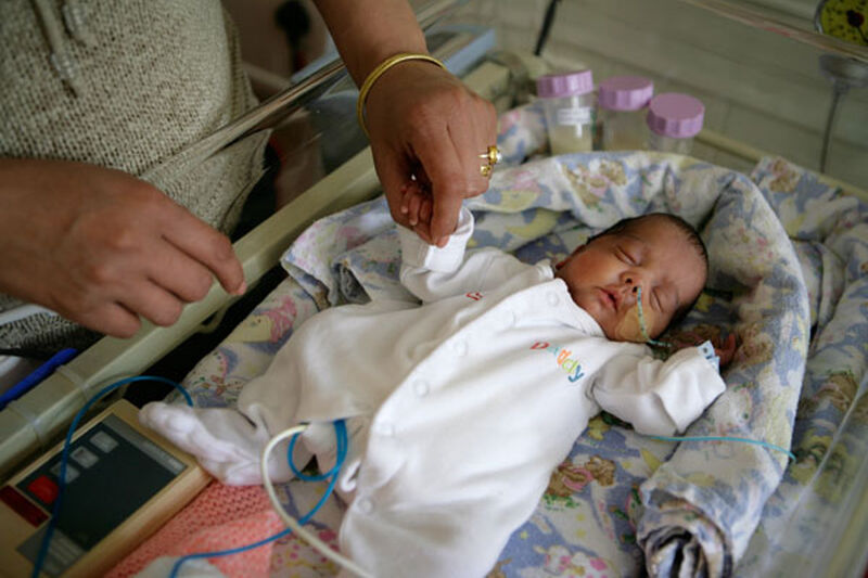 Baby in pyjamas sleeping on its back while parent standing over and holding its hand
