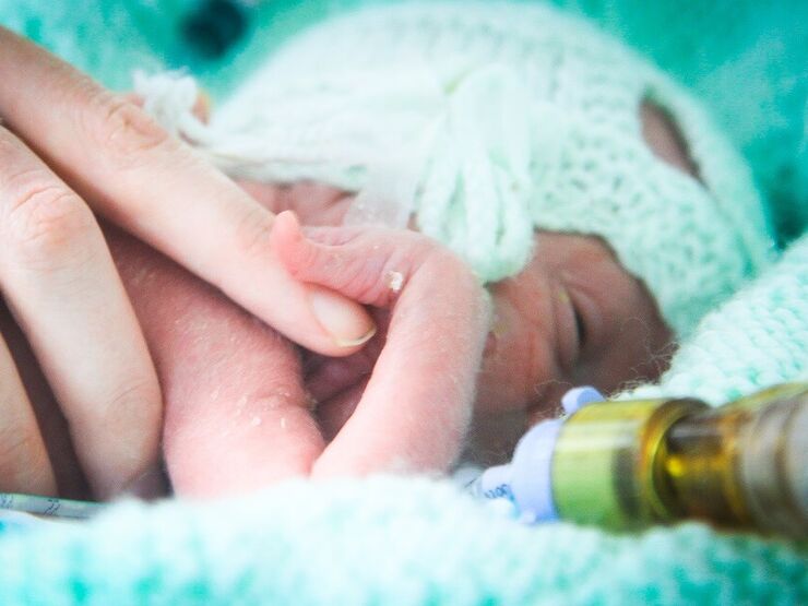 Baby with bandage over its head while holding parents finger