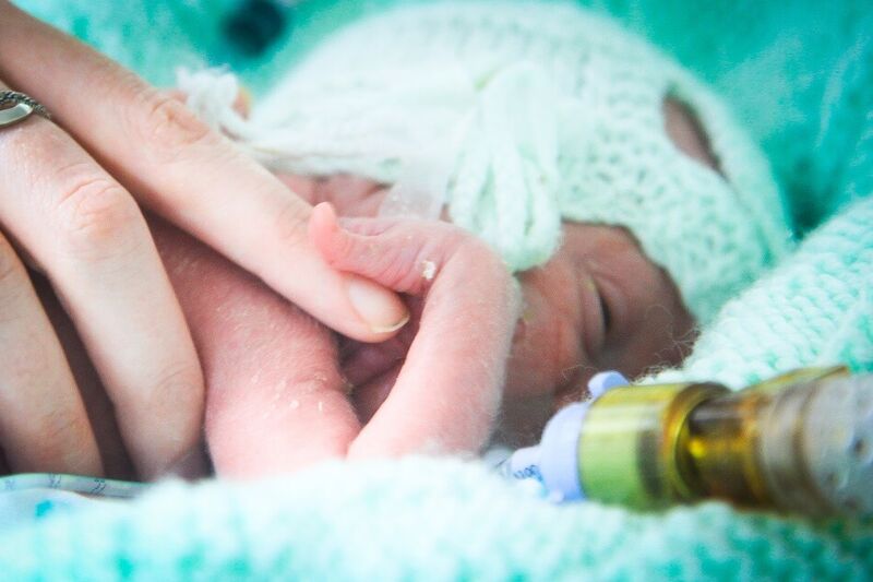 Baby with bandage over its head while holding parents finger