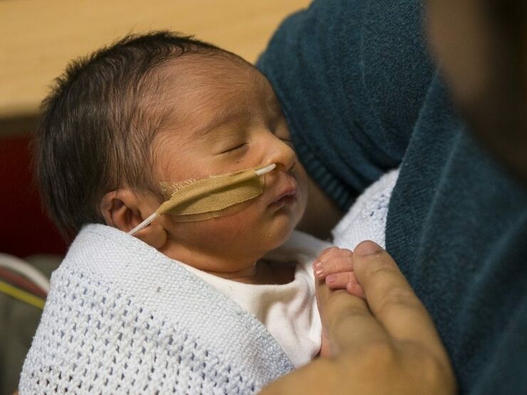 Baby in neonatal care attached to a feeding tube being held by his father