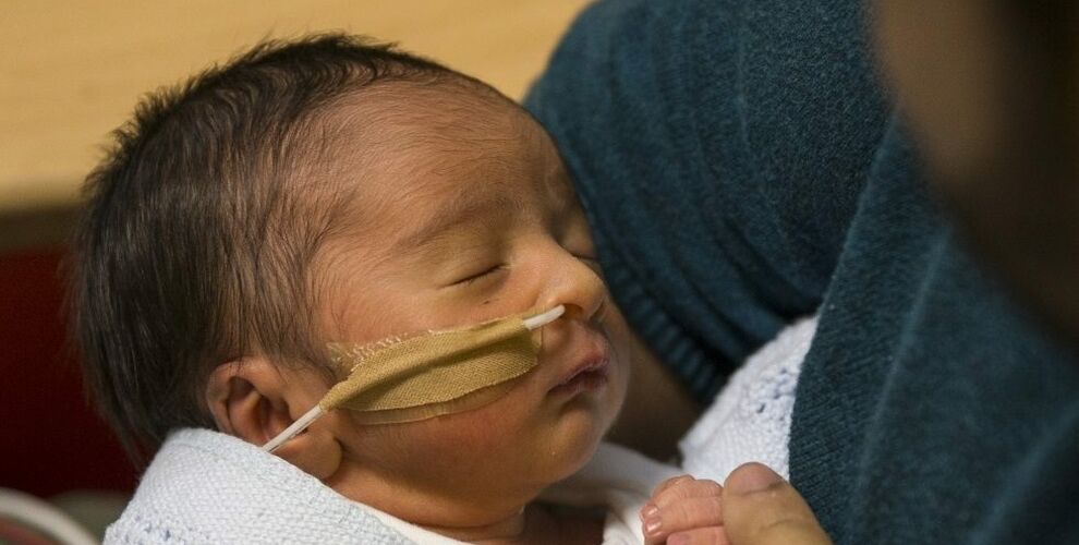 Baby in neonatal care attached to a feeding tube being held by his father