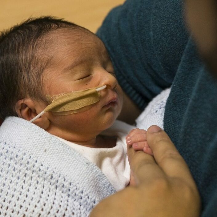 Baby in neonatal care attached to a feeding tube being held by his father