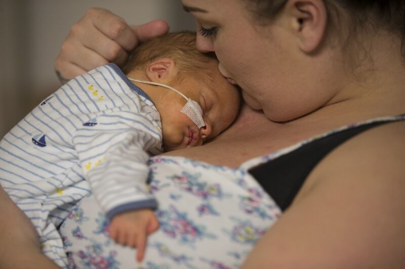 Mum with baby on chest who is asleep and mum is giving the baby a kiss