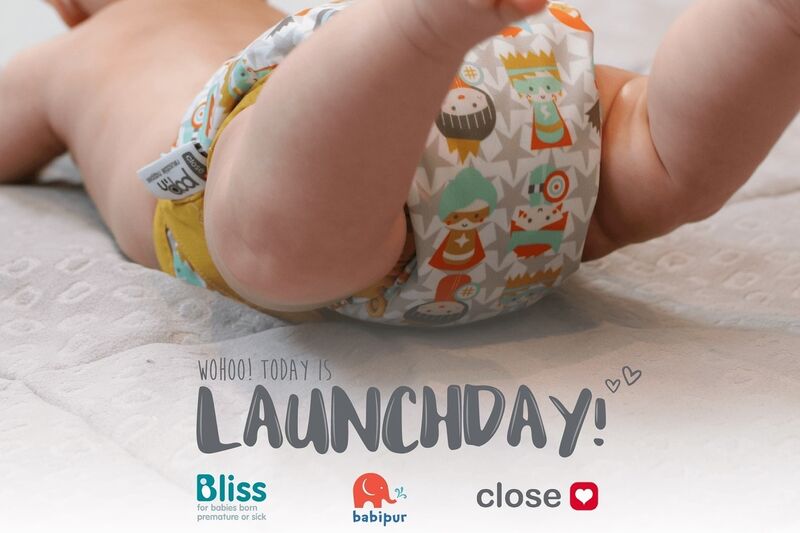 Baby wearing resuable nappy by Close Parent company, with launchday and Bliss and company logos on the image