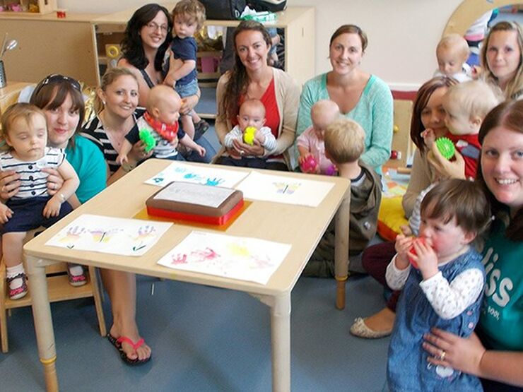 Group of mums and babies with Bliss volunteers sitting around a table in a play area