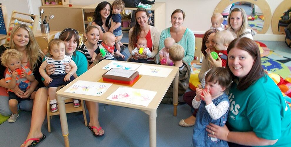 Group of mums and babies with Bliss volunteers sitting around a table in a play area