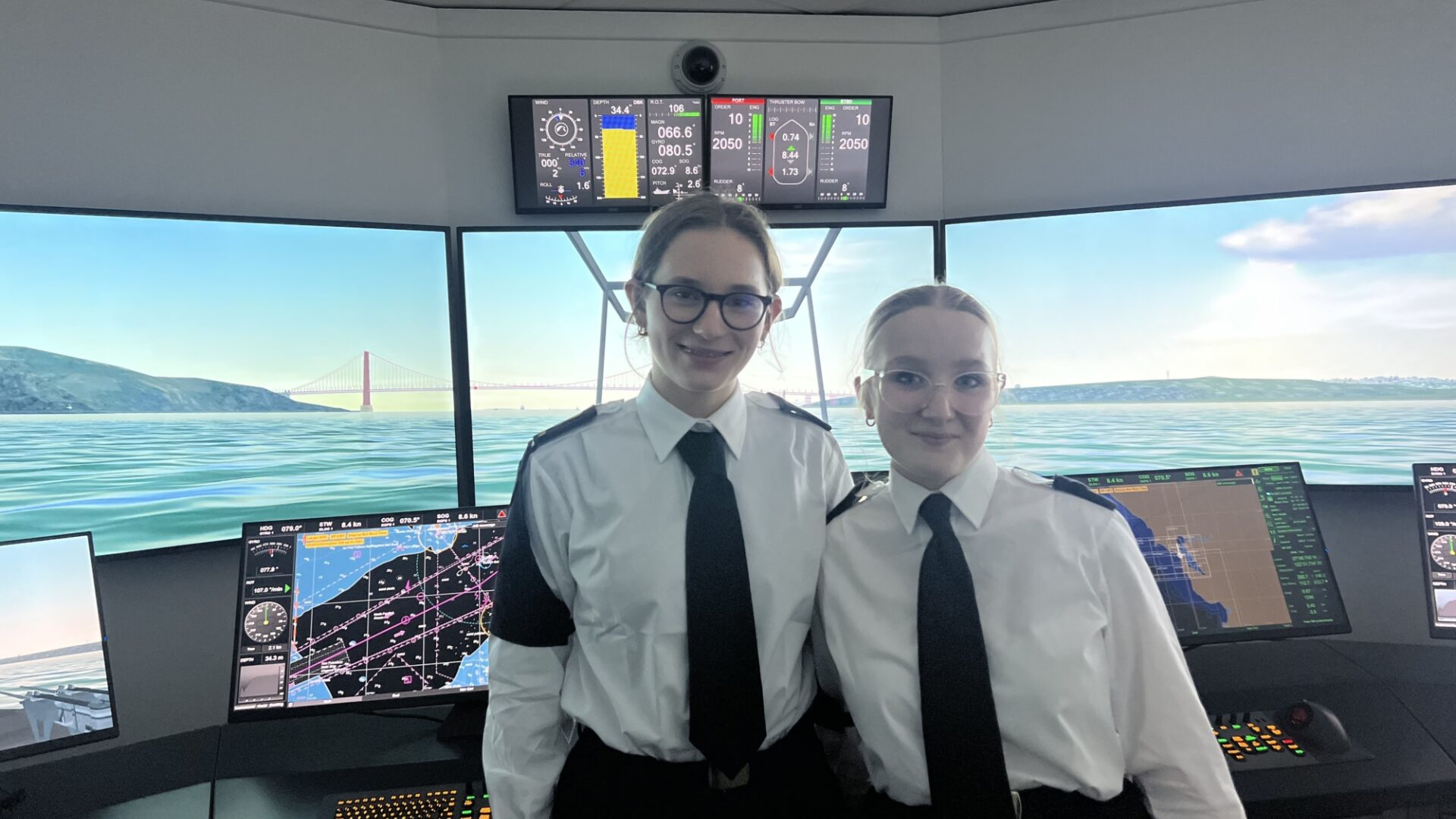 Smiling female cadets from the Royal Navy stand at the helm of a virtual ship they are both smiling and happy