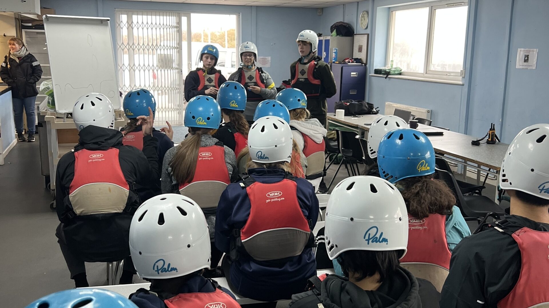 CCF Royal Navy cadets being briefed inside a meeting room. The cadets are wearing safety equipment, ready for an activity.
