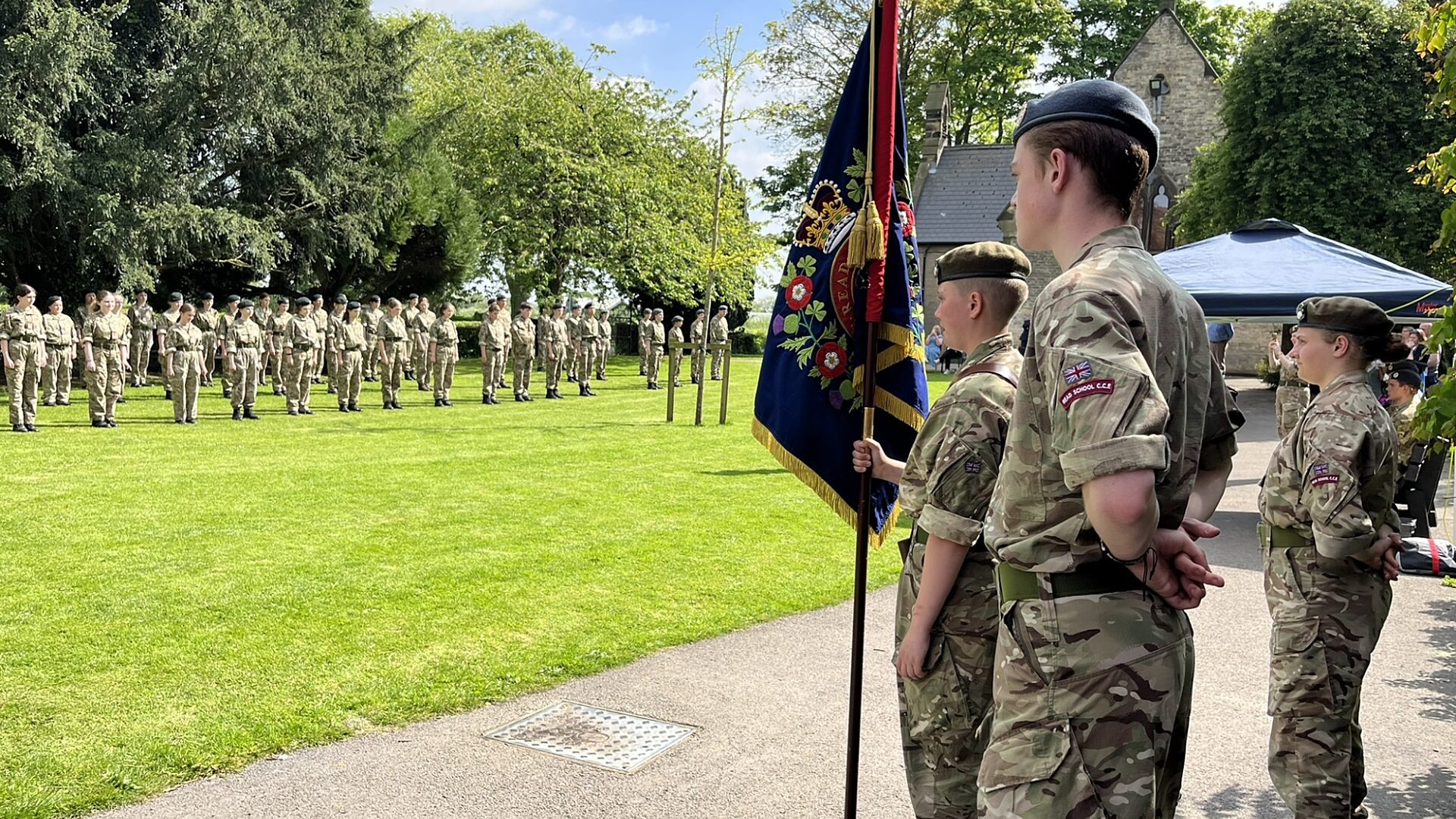 Cadets holding school flag in the forefront with cadets lining up in the background