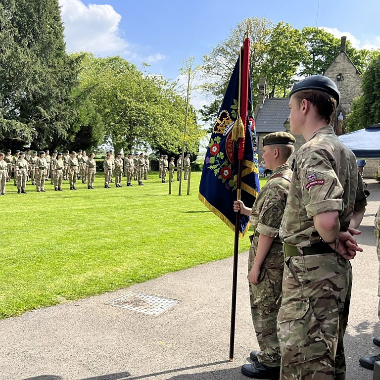 Cadets holding school flag in the forefront with cadets lining up in the background