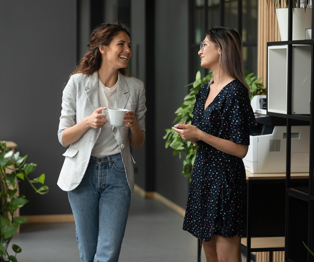 Two colleagues chatting and smiling during a coffee break in a modern office space | Amodaia