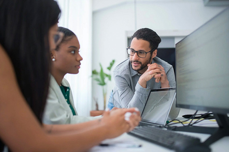 Man mentoring two women while working together on computers in office | Amodaia