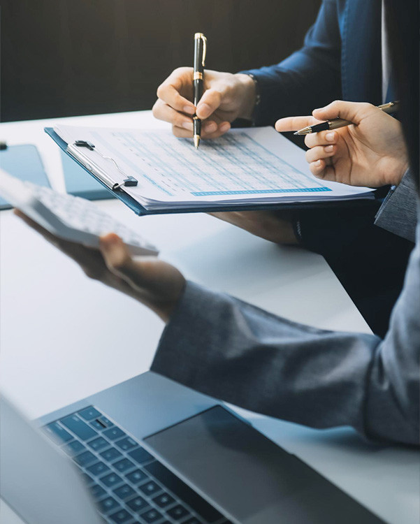 Business professionals reviewing financial documents with a clipboard, calculator, and laptop during a meeting | Amodaia Business professionals reviewing financial documents with a clipboard, calculator, and laptop during a meeting | Amodaia