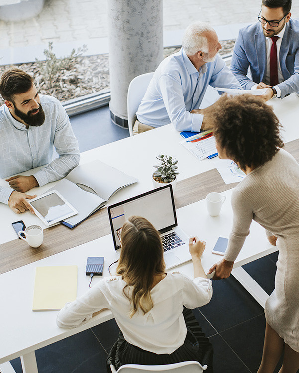 Business team working together at a modern office desk with laptops documents and coffee cups | Amodaia