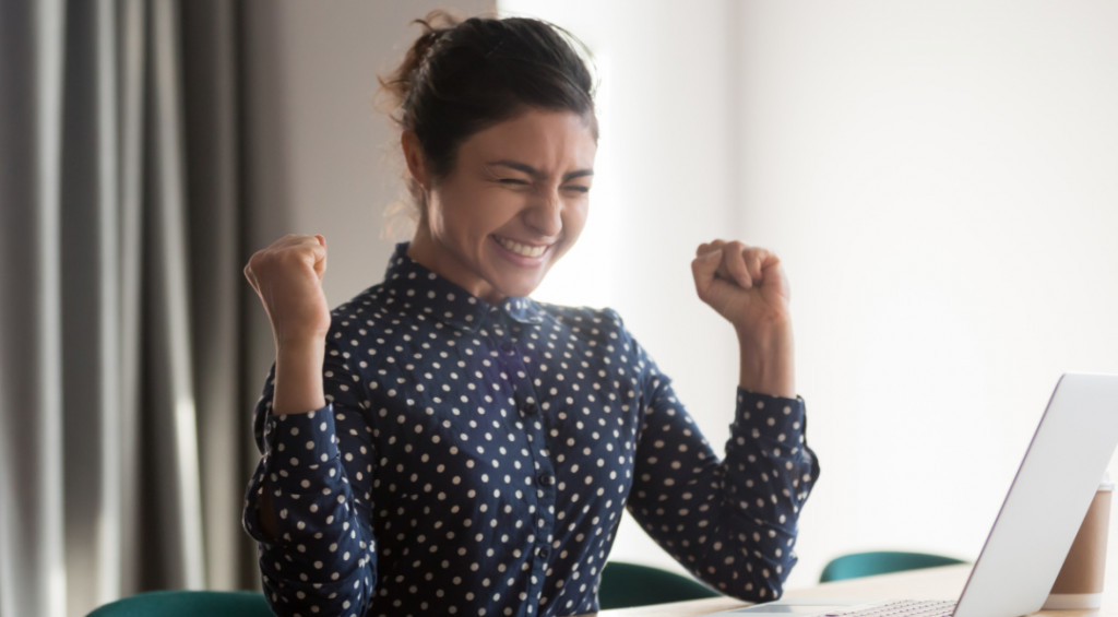 talent success.jpg young woman sitting at laptop smiling and punching air