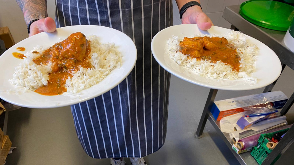Person wearing a striped apron holding two plates of rice served with curry in a kitchen setting | Catherine Beckett Centre