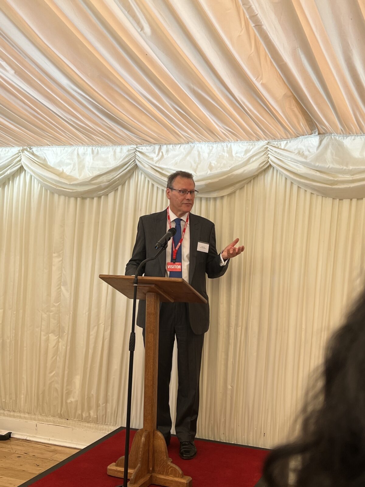 Man in a black suit standing behind a board making a speech.