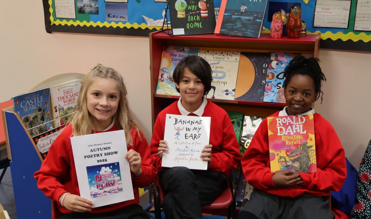 Three children holding up books and smiling at the camera.