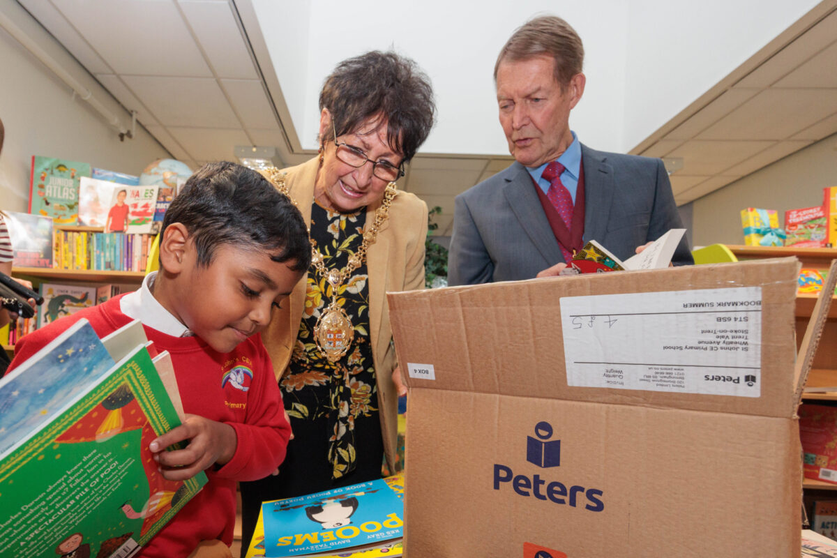 Child, mayor and her assistant, finding books from Bookmark's roots to reading pack. The child is holding a pile of books.
