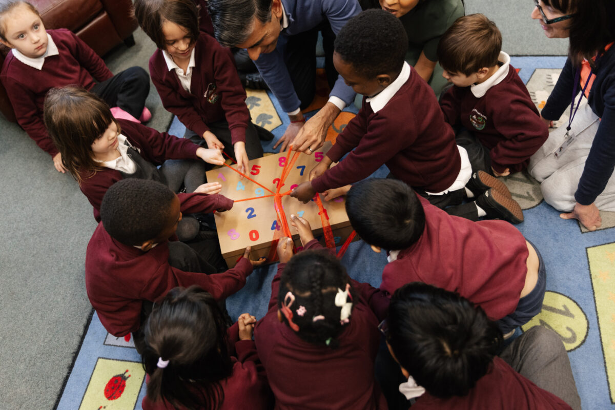 A group of young children sit together on a colourful classroom rug, engaging in a hands‑on learning activity with a numbered Rocket Pack box donated by The Richmond Project.