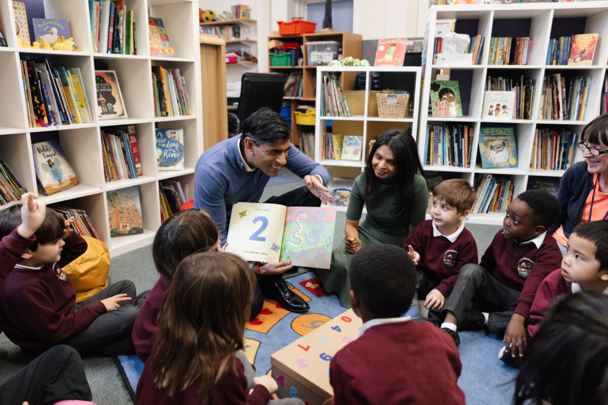Rishi Sunak reads a numeracy book from the Bookmark Rocket Pack to primary aged children who are sat in a circle on the floor.