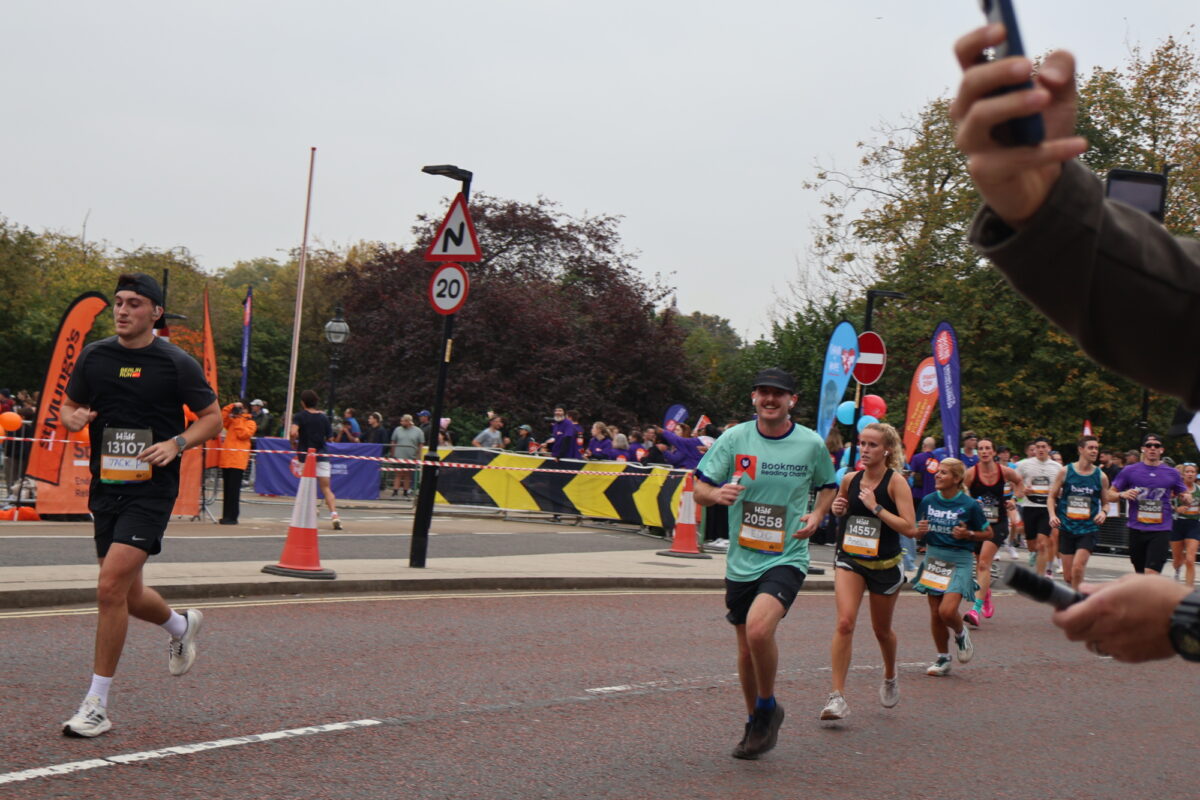 Runner in a turquoise Bookmark t-shirt, smiling at the camera mid-race.