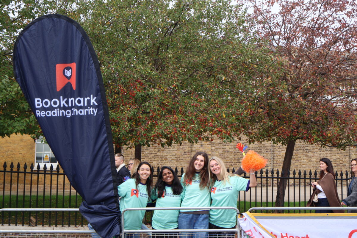 4 women in turquoise t shirts cheering next to a bookmark flag.