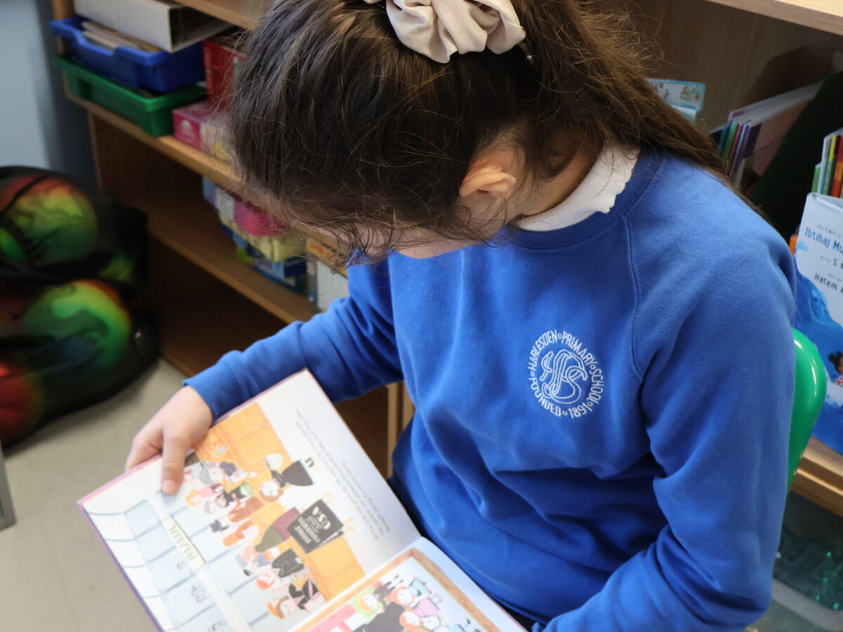 Girl in blue school uniform with a book open on a page.