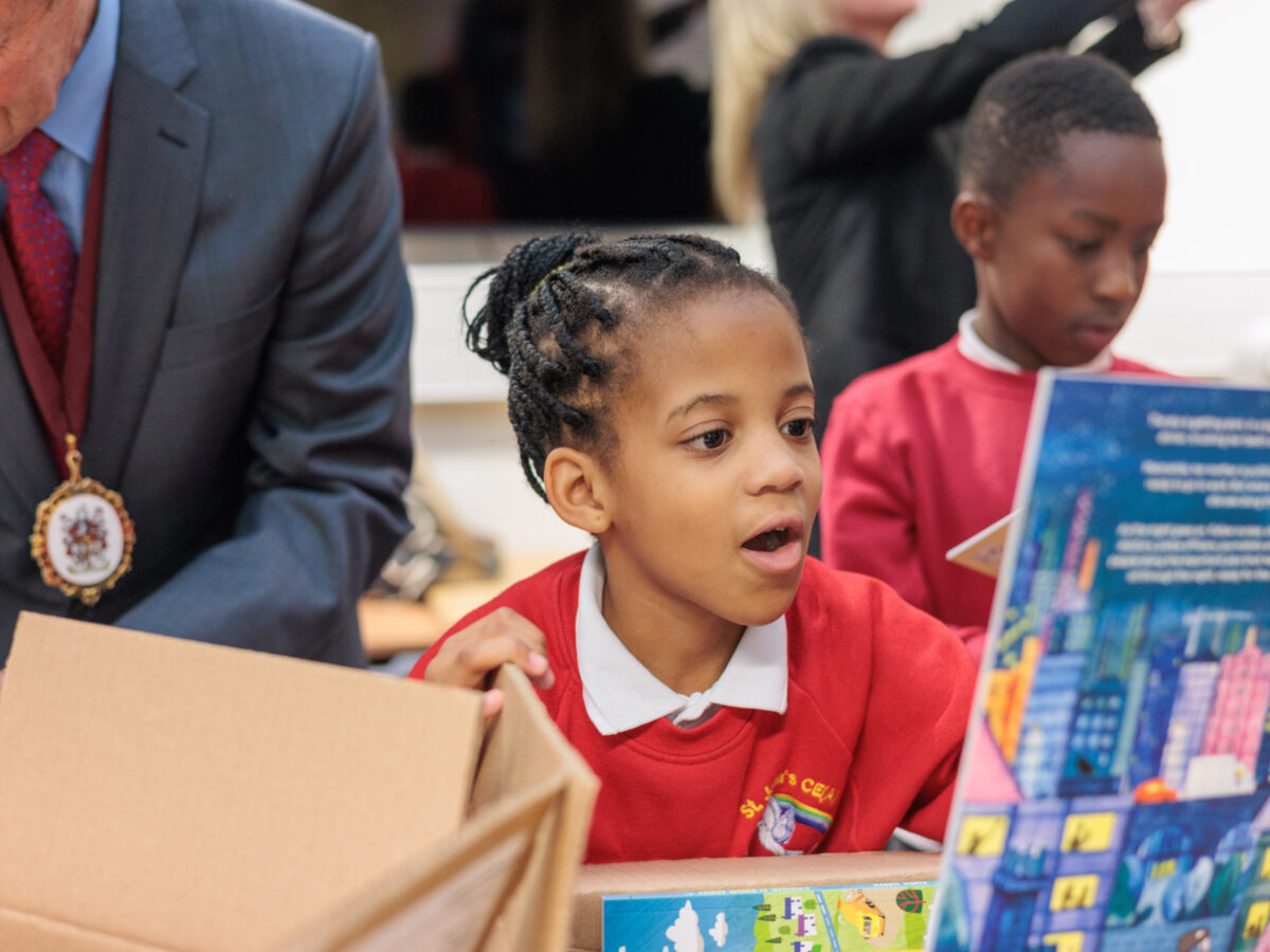 Girl unboxing Bookmark's roots to reading programme pack and looking at a book cover in awe.