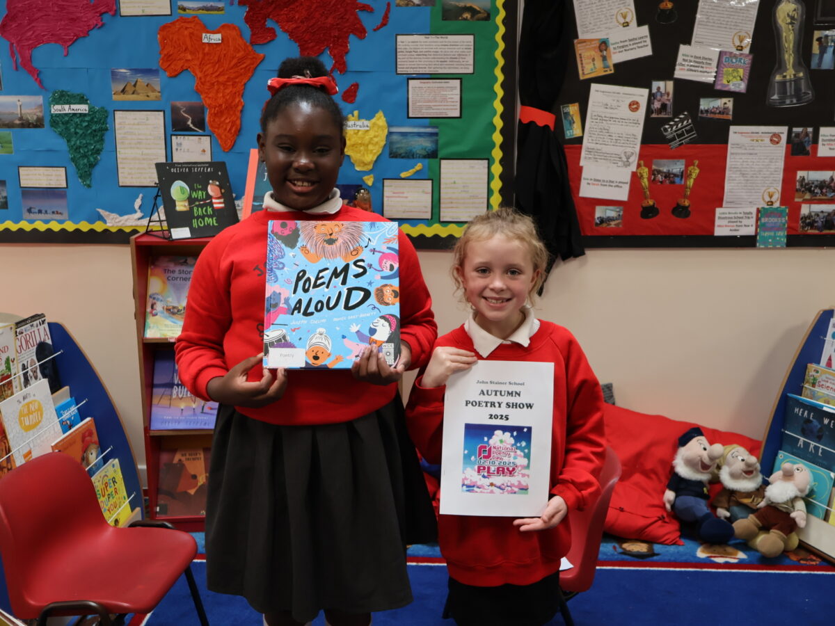 Two pupils in school uniform, holding up books and smiling at the camera