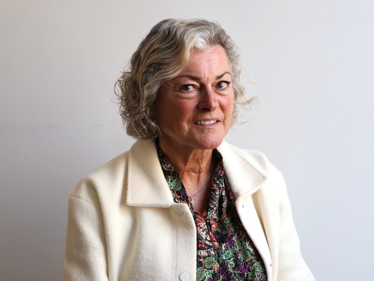 Female wearing a white jacket and a flowery blouse smiling at the camera