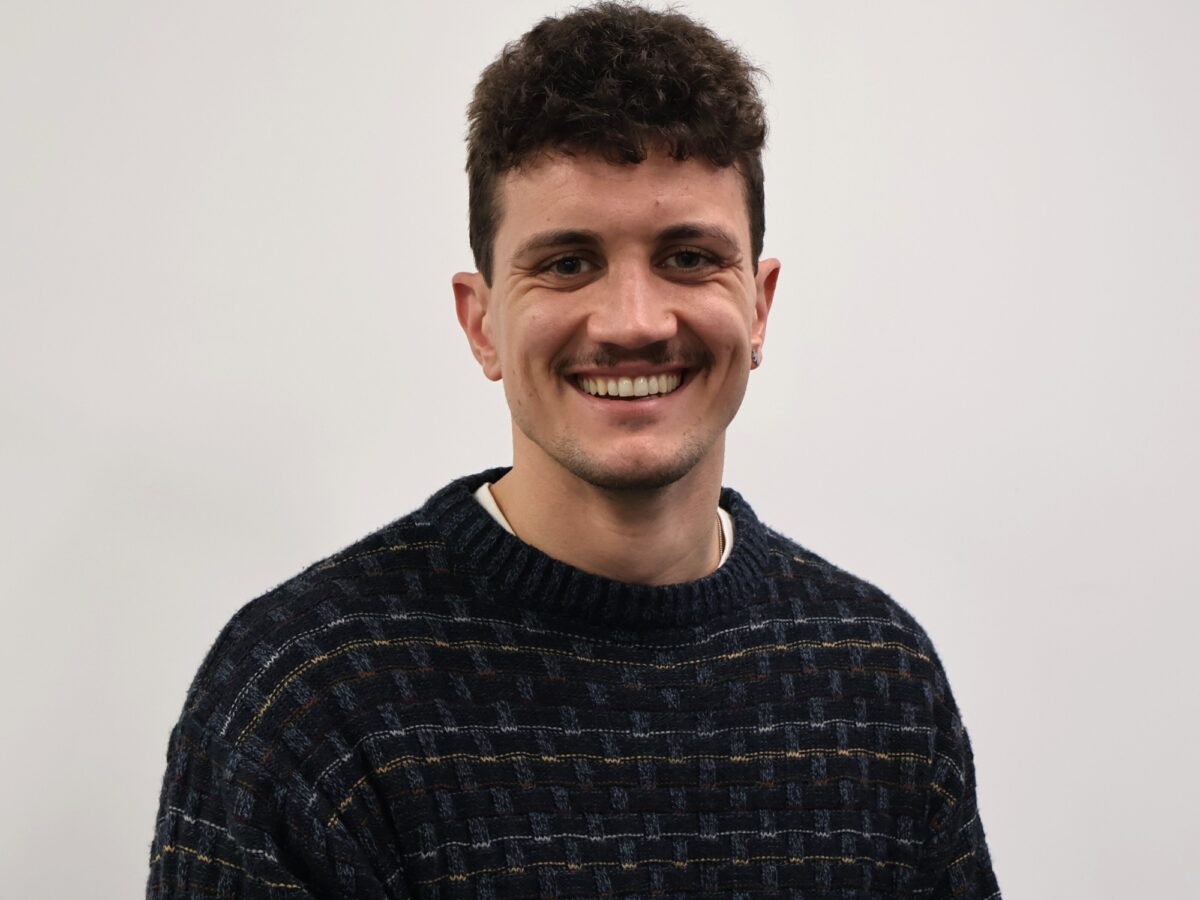 Man wearing dark blue jumper and brown hair, smiling at the camera