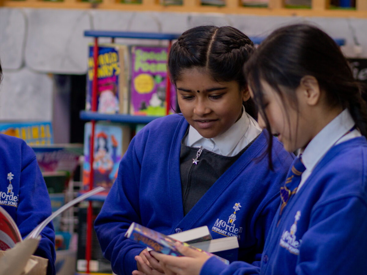 two pupils standing next to each other looking at a book with a smile