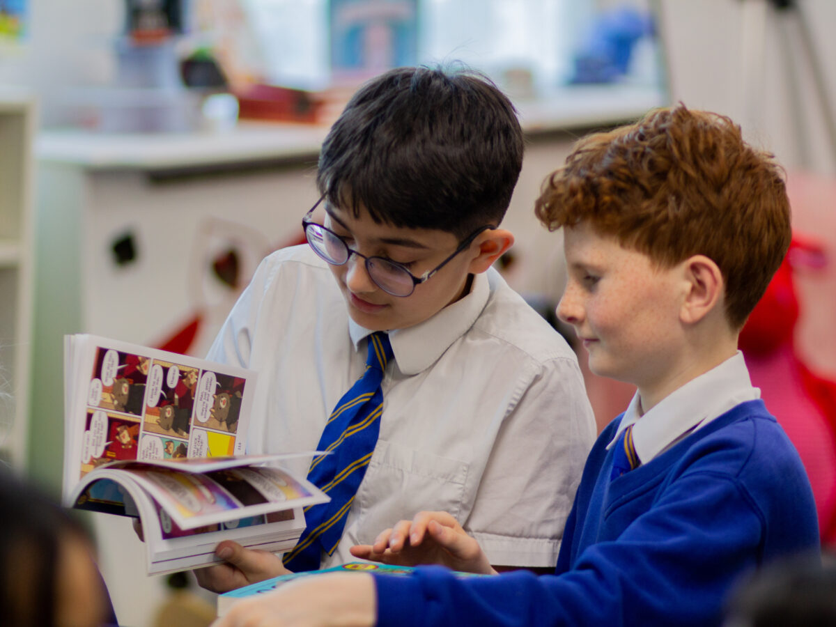 Students at Morden Primary School reading books from the Roots to Reading programme during a classroom visit, sitting together and engaging with illustrated storybooks as part of a literacy and reading‑engagement session