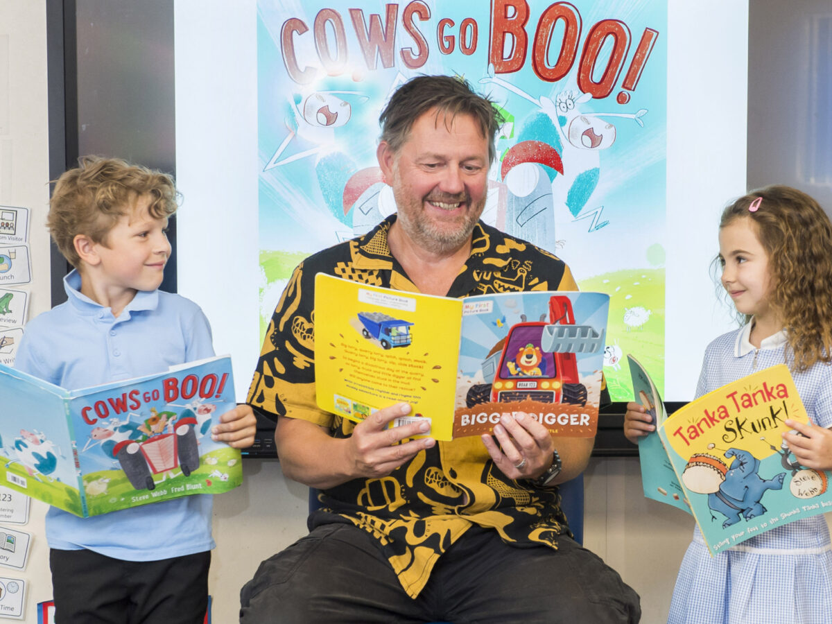 A man sits between two young children, a girl and a boy. All three are holding up picture books