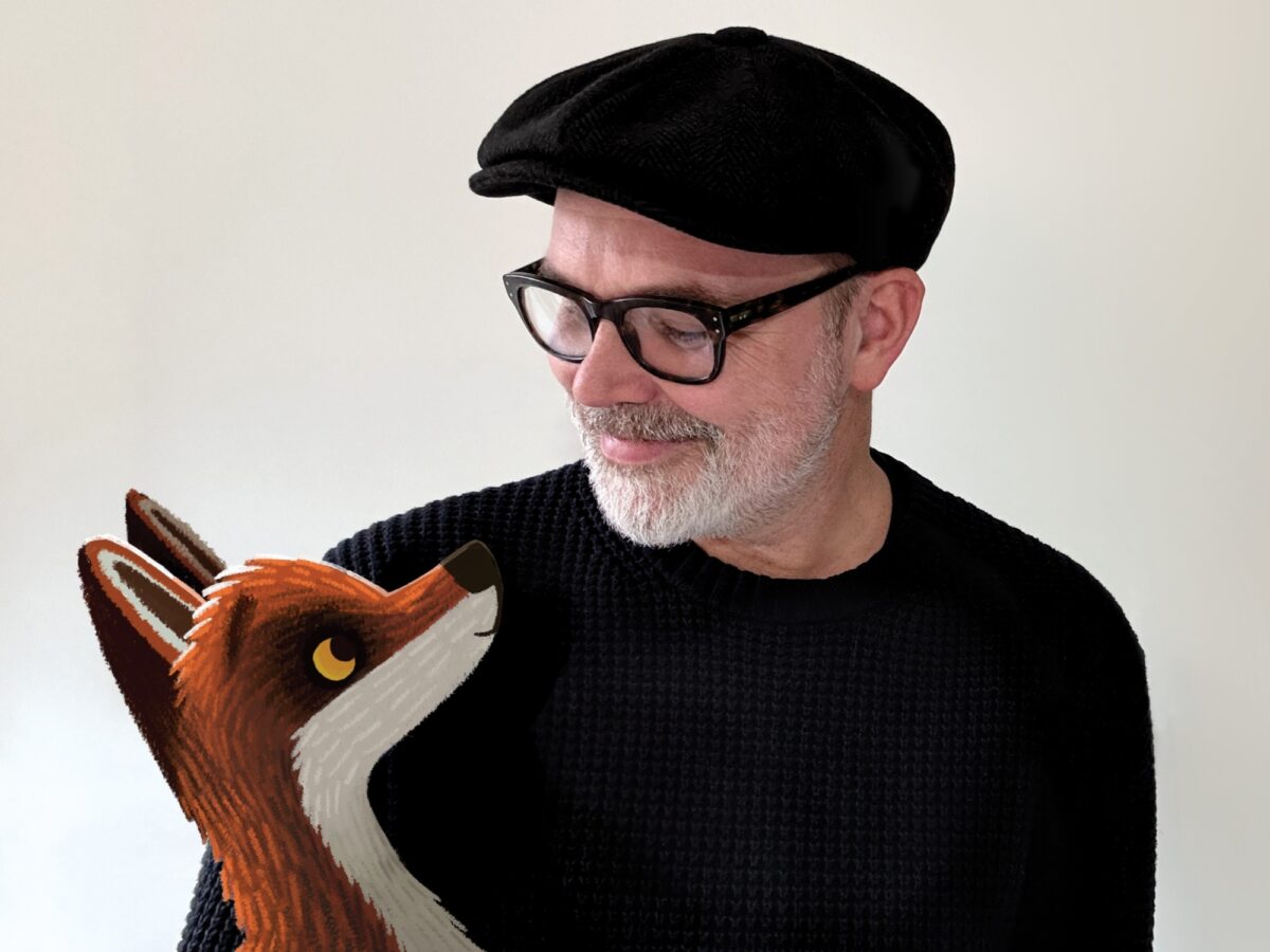 A man wearing a black jumper and a black hat looks down at a cartoon drawing of a fox, edited onto the picture.
