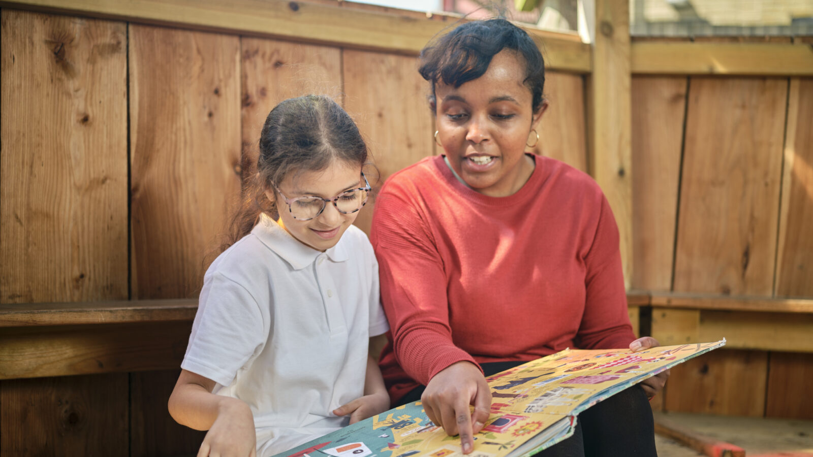 Child reading a book with their Bookmark reading volunteer in an outdoor reading area.