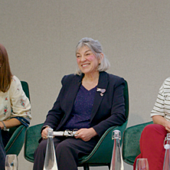 Alison David is in the center at a Mind the Gap panel event wears a dark blazer over a patterned top and holds a small object in their hands.
