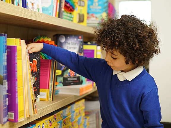 Child with curly brown hair looking through a shelf full of books