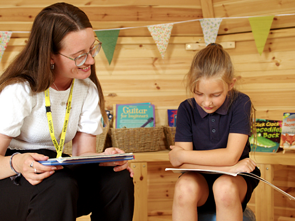 A woman reads a story book with a little girl in a wooden panelled room