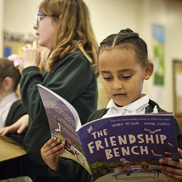 A young girl reads a picture book that is held out in front of her.