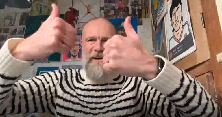 Olaf Falafel wearing a black‑and‑white striped sweater gives two thumbs up in a  room decorated with colourful artwork and posters.