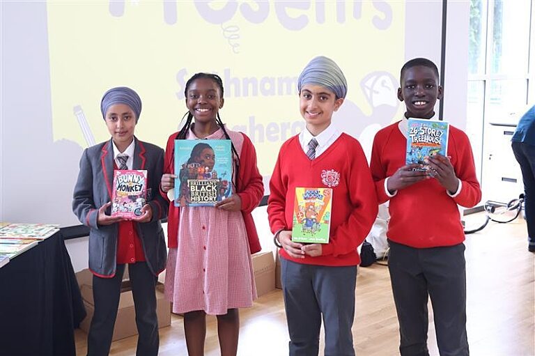 Four children in a school hall smiling holding a book of their choice in front of them