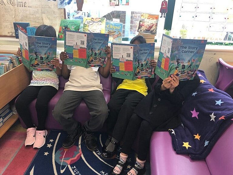 Four children sat on a sofa with The Story Corner Magazines open in front of their faces