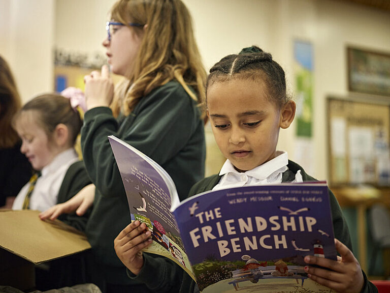 A young girl reads a picture book that is held out in front of her.