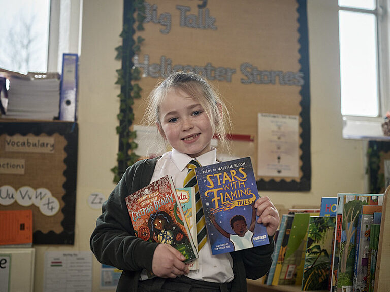 A girl in school uniform holds up 3 books and smiles