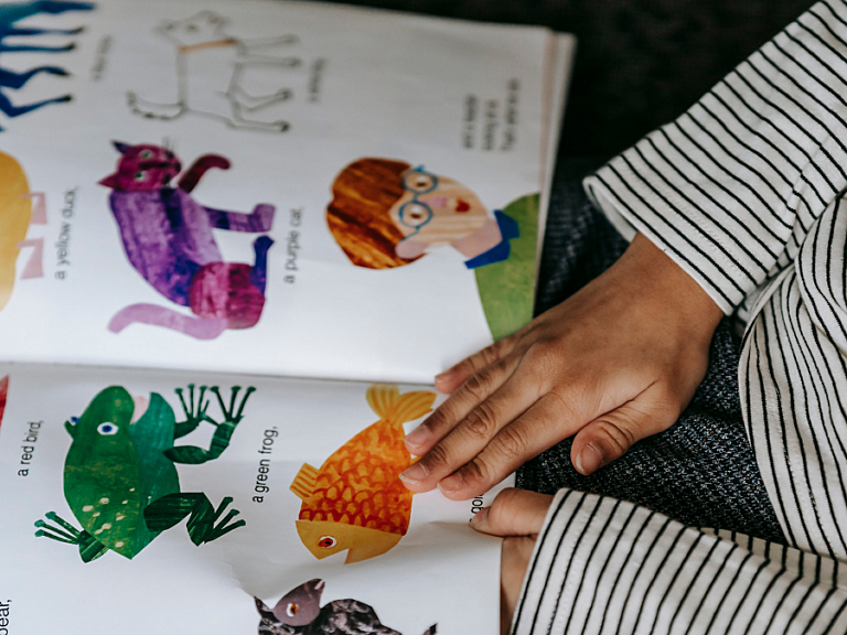 A child's hands turning the pages of an illustrated animal picture book.